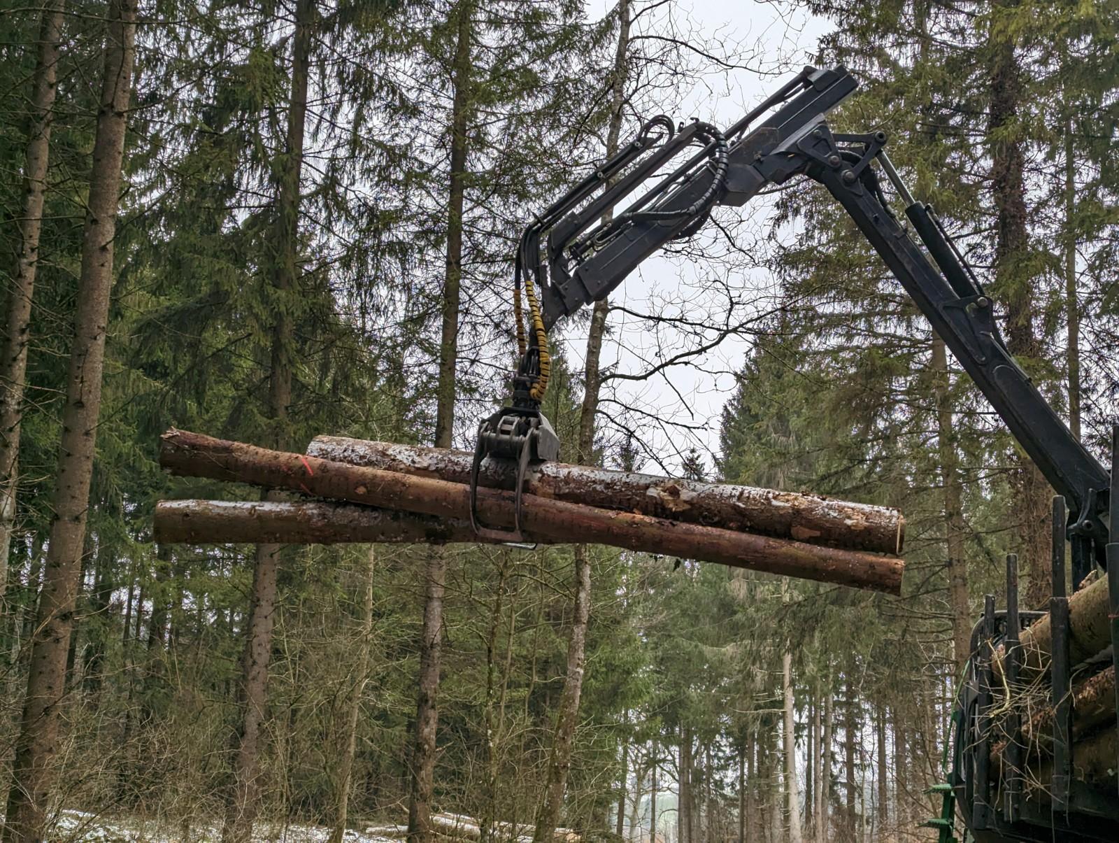 Rückewagen im Wald. Zu sehen ist die Zange des John Deere 1110 der Baumstämme hochhebt